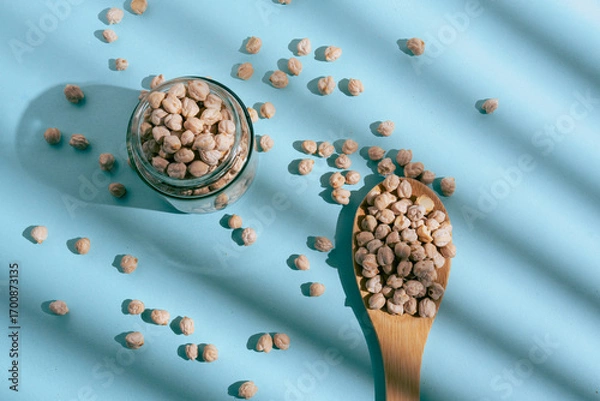 Obraz Barley grains scattered from a glass jar on a blue background. Blue background and minimalist style, soft shadows and natural light. 