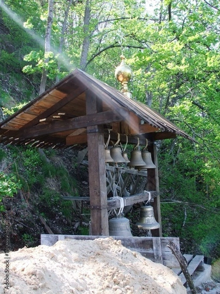 Fototapeta Wooden bell tower with multiple bells surrounded by green forest  