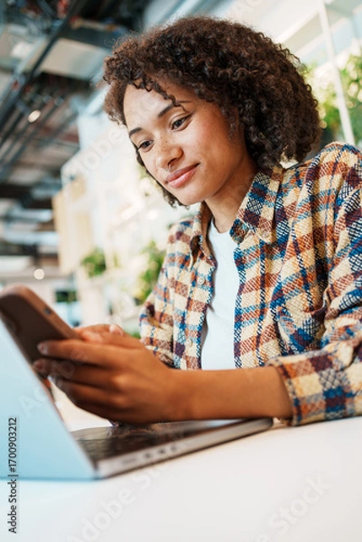Fototapeta A young woman interacts with technology in a modern workspace, enjoying a cheerful atmosphere