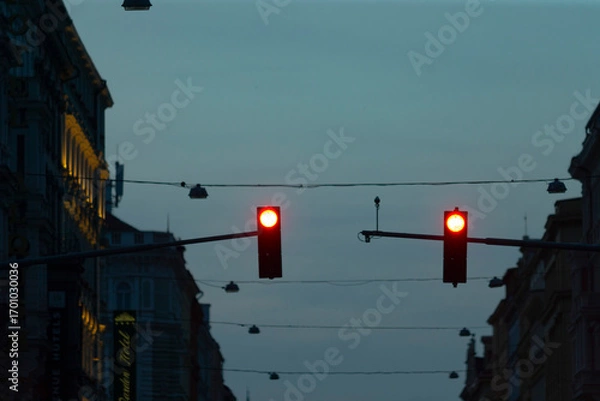 Fototapeta Bright red traffic lights glow in the twilight of an urban street scene, clearly signaling to vehicles that they must come to a complete stop in the busy city environment during dusk hours