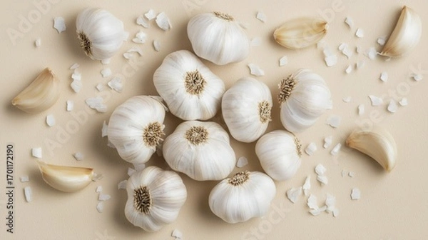 Fototapeta Fresh garlic bulbs and cloves with salt flakes on a beige surface.