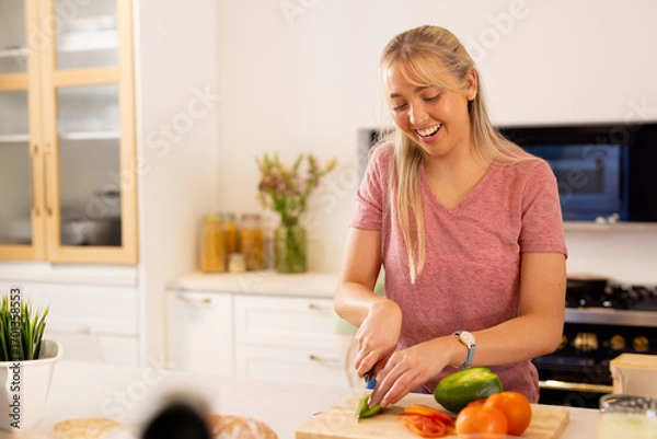 Fototapeta Woman slicing green bell pepper on cutting board at kitchen island, with knife, copy space