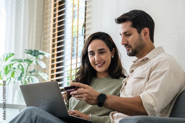 Fototapeta Happy couple using credit card and laptop at home for seamless online shopping experience with smartphone