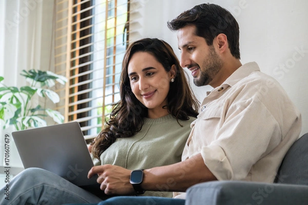 Fototapeta Hispanic couple using computer watching social media and streaming show together at home on the sofa