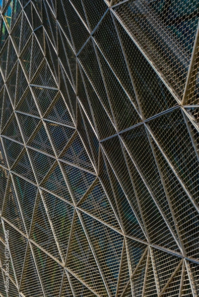 Fototapeta a modern architectural facade, featuring a complex lattice of triangular metal frames. a geometric pattern of shadows and highlights