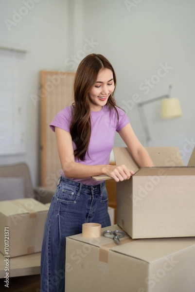Fototapeta Asian Woman Packing Moving Boxes in New Home Apartment Smiling Young Female Relocating Belongings Happy with House Relocation Moving Day Preparation