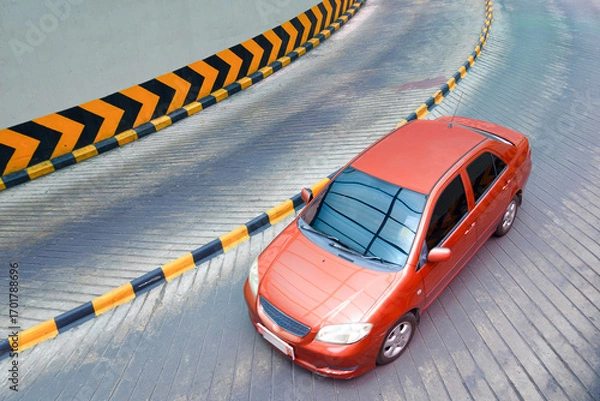 Fototapeta A red car is moving slow down on curve way into the underground parking lot of shopping mall, High angle view with copy space