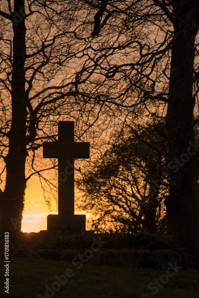 Obraz Ancient cross tombstone silhouetted at sunset