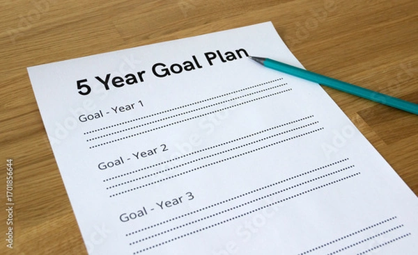 Fototapeta Close up of a paper sheet that says '5 Year Goal Plan' with a pencil pointing at the headline, isolated on wooden background