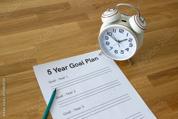 Fototapeta sheet '5 Year Goal Plan' with an alarm clock standing on it on a wooden table