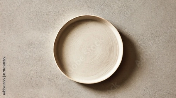 Obraz Top-down view of an empty beige ceramic plate with a textured surface on a neutral grey background.