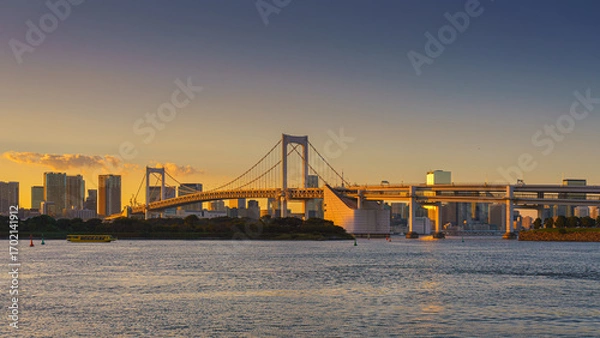 Fototapeta Tokyo, Japan - Oct 13 2024, panoramic view of Tokyo Bay with a cable-stayed Rainbow Bridge above it, a boat and a water bus sailing, at sunset, Tokyo, Japan