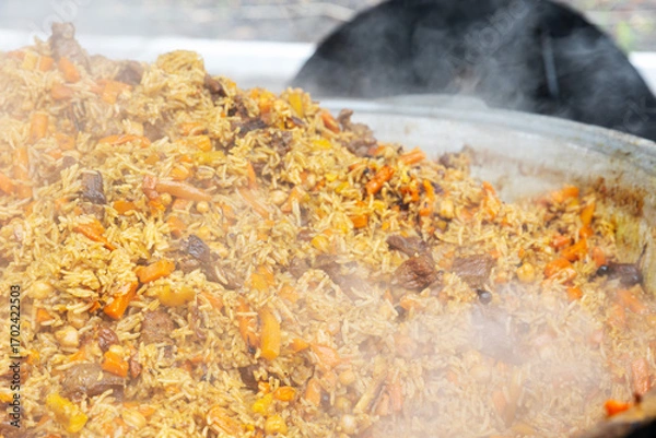 Fototapeta Central Asian plov or pilaf cooking in a large cauldron, steaming and ready to serve