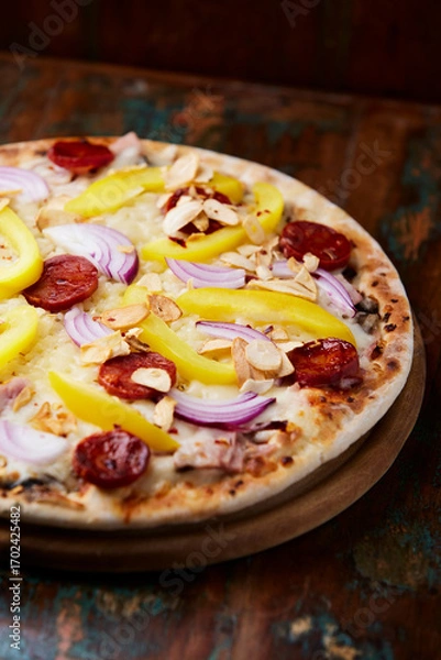 Fototapeta Pizza with chorizo ​​sausage, mozzarella cheese and yellow pepper. Rustic wooden background. Soft focus.	