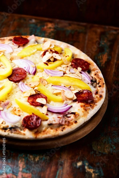 Fototapeta Pizza with chorizo ​​sausage, mozzarella cheese and yellow pepper. Rustic wooden background. Soft focus.	