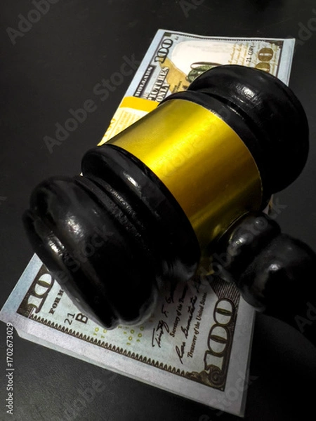 Fototapeta A judges gavel rests on a stack of 100 dollars bills.