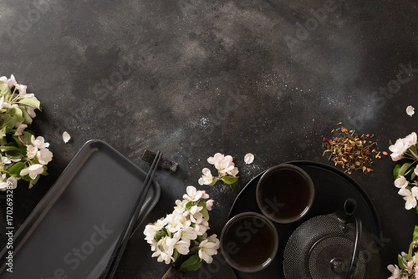Fototapeta Black tea, cast iron kettle and blossom white flowers. Vertical composition with sakura bloom and petals. Japanese style and tea ceremony. Top view.