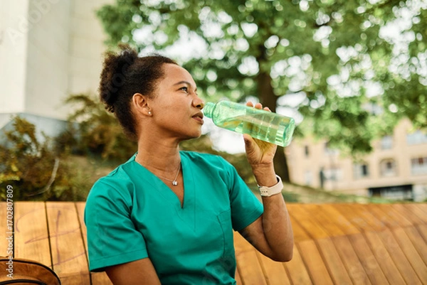 Fototapeta Young woman or a nurse or a doctor during office hours break enjoying a fresh salad and drinking water in a park during a sunny day while smiling and relaxing on a bench