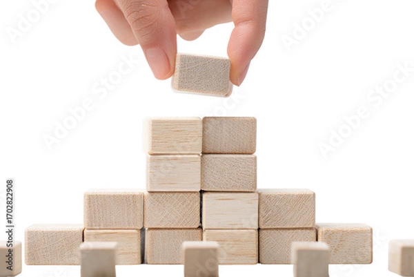 Obraz A hand carefully places a light beige wooden block atop a growing stack of similar blocks.  The blocks form a small pyramid-like structure