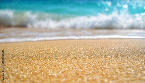 Fototapeta Close-up view of tropical beach sand with turquoise ocean waves crashing gently in background under clear blue sky. Soft, textured