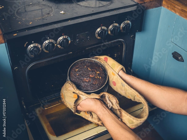 Obraz Man removing burnt cake from the oven