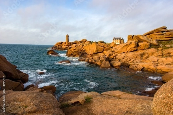 Fototapeta Scenic view of the Ploumanac'h lighthouse on the Pink Granite Coast in Brittany, France. Waves crash on the unique reddish rocks during golden hour. Famous travel destination in Europe.