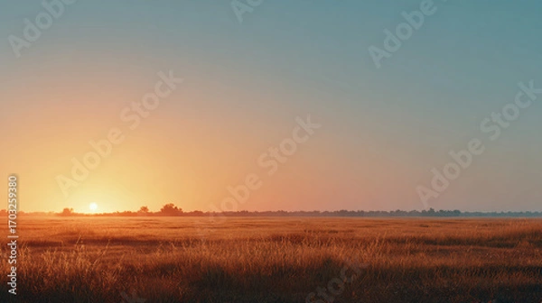 Fototapeta wide open field with warm orange glow at sunset, smooth clear sky transitioning from orange to pale blue, minimalist summer dusk scene with ample negative space