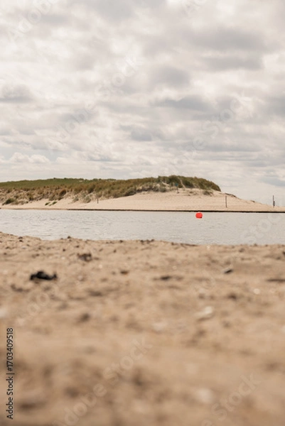 Fototapeta Bright sandy shoreline with calm water reflecting clouds in a coastal setting during daytime