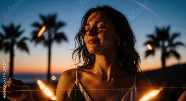 Fototapeta A woman is centered against a twilight backdrop of palm trees, eyes closed. She wears a tank top and is illuminated by warm light flares.

