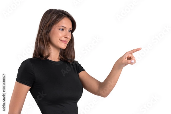 Fototapeta Smiling woman pointing with index finger while standing isolated on white background in cut-out style, wearing casual outfit, showing direction gesture.