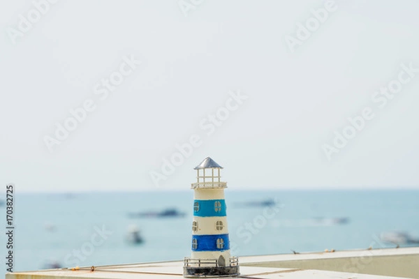 Obraz Small lighthouse model on the table with sea background