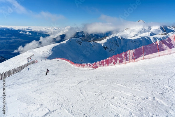 Fototapeta A red fence along a ski track with a view of the mountains.