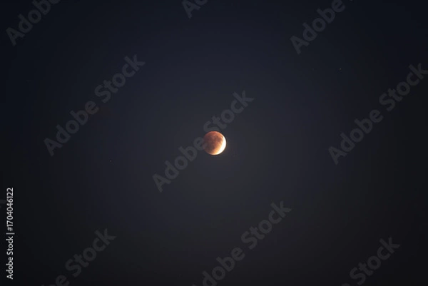 Fototapeta A beautiful lunar eclipse creates a striking reddish hue on the moon, showcasing the wonders of the universe against a clear, dark backdrop. Stargazers admire the celestial phenomenon