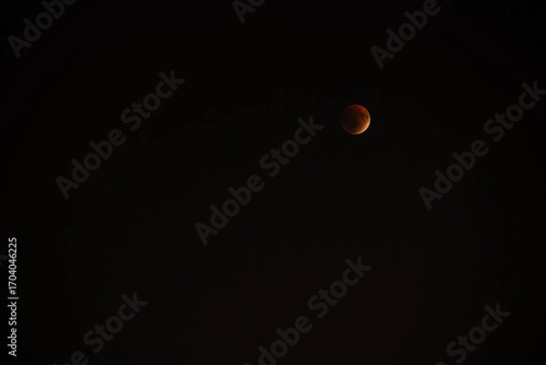 Fototapeta In a clear night sky, a mesmerizing partial lunar eclipse displays a reddish hue on the moon. Stars twinkle softly in the background, accentuating the celestial beauty above