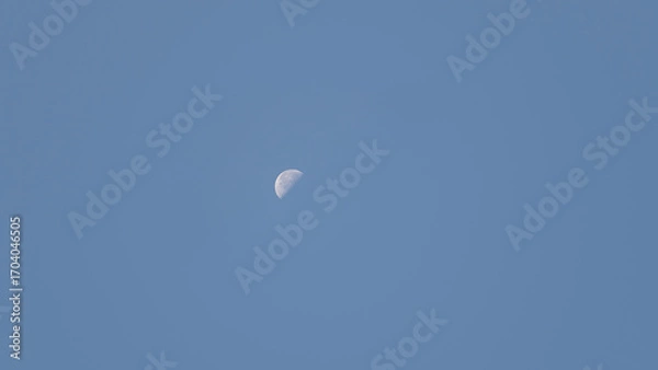 Fototapeta A crescent moon hangs in a bright blue sky as daylight persists in the late afternoon. The tranquil atmosphere invites reflection and appreciation of nature's beauty