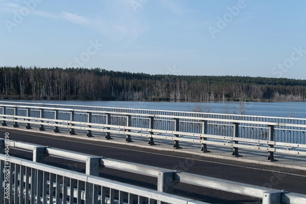 Fototapeta A bridge crosses a serene lake, reflecting the clear sky and bordered by lush greenery. The peaceful setting invites relaxation and contemplation