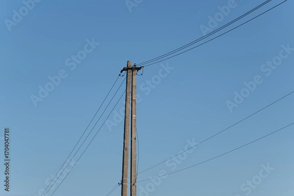 Fototapeta A tall utility pole reaches high with power lines stretching across the bright blue sky in a peaceful rural landscape during the afternoon hours