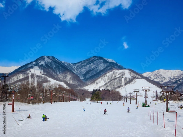 Fototapeta Winter landscape from the base of a ski slope with a view of snowy mountains and visitors (Tsugaike Kogen, Hakuba, Nagano, Japan)