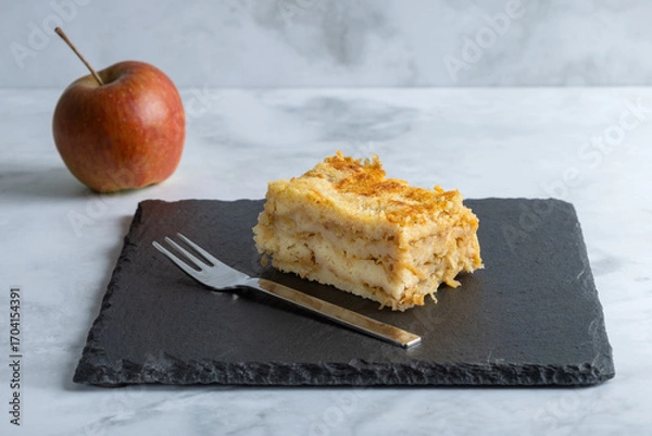 Fototapeta Moist layered apple semolina pie with crispy golden topping, an apple and fork.