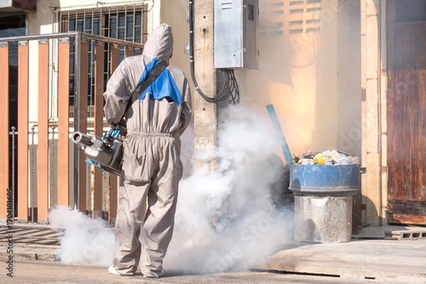 Fototapeta Healthcare worker using fogging machine spraying chemical to eliminate mosquitoes in drainage ditch between two houses.