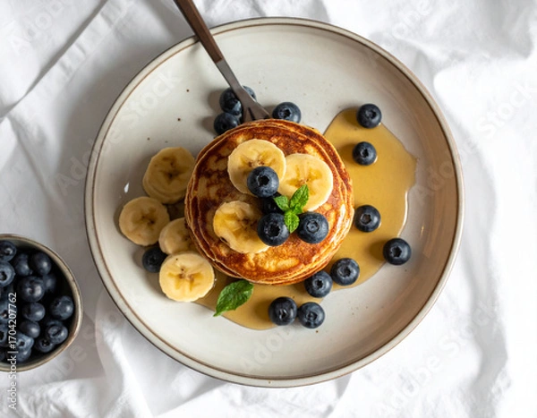 Fototapeta Banana Pancakes with Blueberries and Maple Syrup on Ceramic Plate
