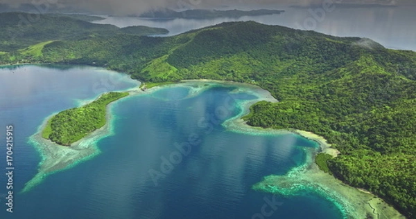Fototapeta Fiji islands: Aerial view of tropical islands with lush green vegetation reflecting on the turquoise ocean water under a cloudy sky. Wild nature travel landscape. Drone flight