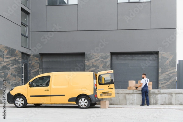 Fototapeta Courier loading cardboard boxes into a delivery van