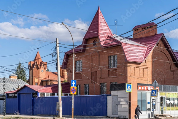 Fototapeta Brick house in Hanseatic style with pointed gabled roofs and arched details. Street scene with a pedestrian and road signs under a clear sky.