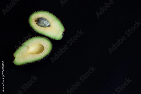 Obraz Avocado halves on a dark black background, arranged in the corner of the frame. Minimalist food composition, top view.