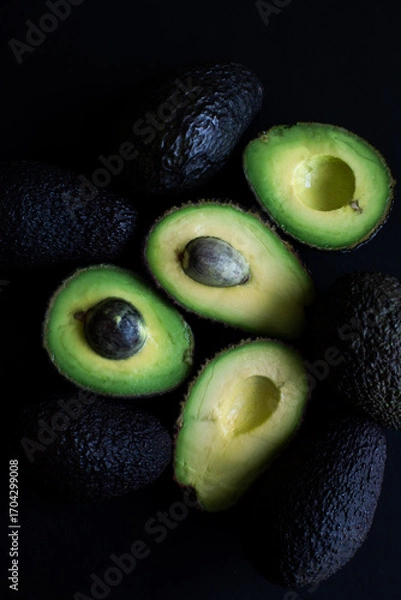 Obraz Fresh whole and cut avocados on a dark background. Healthy vegan food, rich in nutrients and healthy fats.
