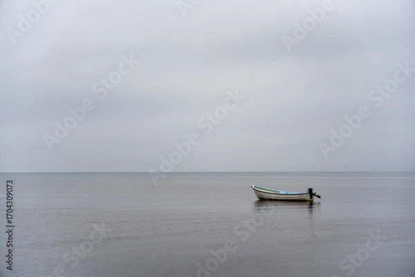 Fototapeta Small Boat on a Calm Sea - Minimalist Solitude on a Gray Day