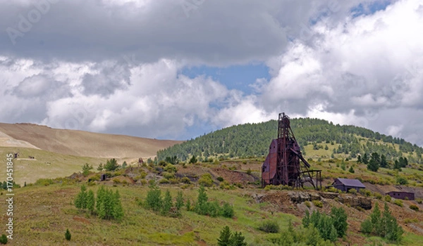 Fototapeta Equipment remains of 19th Century deep gold mining operations near Victor, Colorado, U.S.A. with spoil from the current Cripple Creek Mining District open cast gold mine in the background