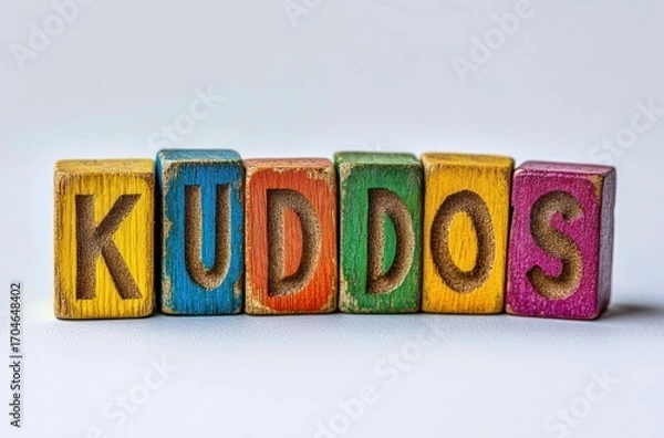 Fototapeta Colorful wooden blocks spelling the word kuddos arranged in a row on a white surface