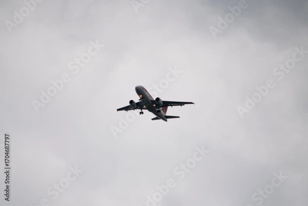 Fototapeta Photograph of an airplane flying in cloudy skies, about to rain